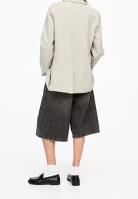 Jasnoszary oversize'owy żakiet, ciemnoszare dżinsowe kuloty, czarne mokasyny i białe skarpetki. Posiada luźny krój i postrzępione wykończenie na szortach.