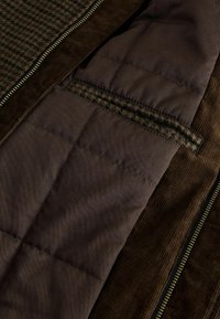 Brown quilted fabric interior with a houndstooth pattern on the left side. Vertical corduroy texture edges and gold zipper detail visible.