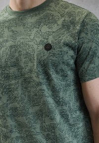 Zielony t-shirt w wzory, z krótkimi rękawami, okrągłym dekoltem oraz teksturowanym wzorem z abstrakcyjnymi kształtami; zawiera małe czarne logo.