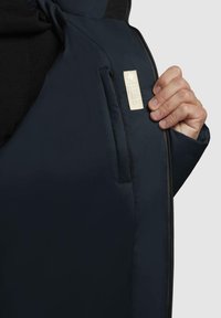 Giacca blu navy realizzata in tessuto liscio, dotata di chiusura con zip e una etichetta cucita con dettaglio in rilievo nella zona tasca.