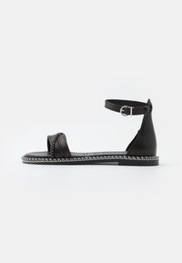 Black leather sandal with a flat sole, ankle strap, and decorative stitching along the edge. Open toe design and minimalistic style.