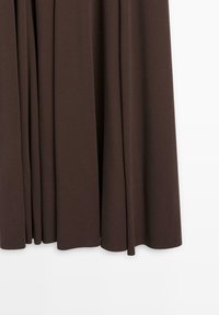 Jupe en tissu marron à la texture lisse, avec des plis amples et un design fluide. Le tissu tombe délicatement jusqu'au sol.