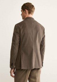 Brown blazer featuring a classic design, tailored fit, and textured fabric. Back view shows a single vent and buttoned cuffs.