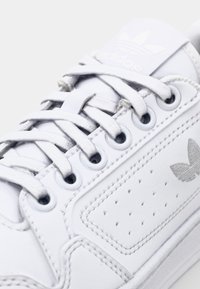 Zapatilla blanca con parte superior de cuero suave, detalles perforados, cordones planos y logo bordado. Presenta una lengüeta acolchada y ojales reforzados.