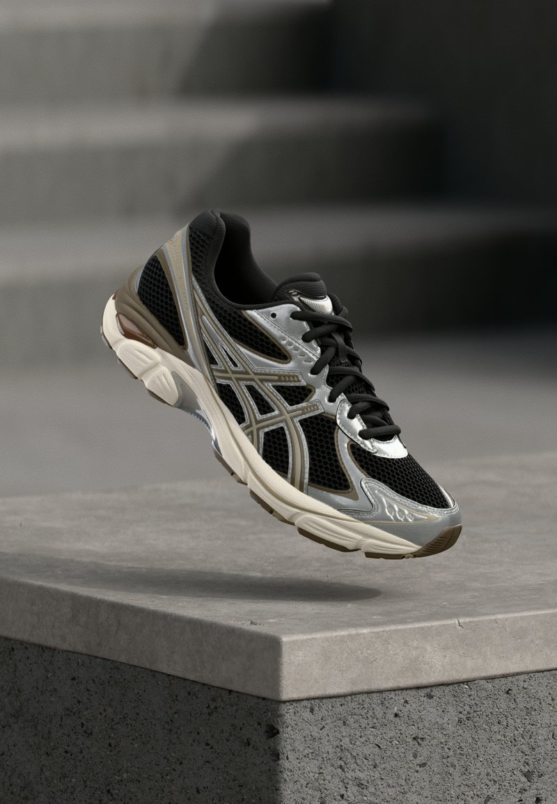 Black and silver running shoe with mesh and synthetic materials, featuring textured patterns and a cushioned sole. Stylish lace-up design.