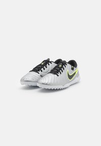 Silver athletic shoes with a textured upper, black laces, and a yellow-green Nike swoosh. Features a rubber outsole for traction.
