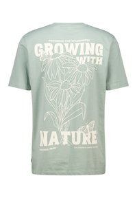 Mintt vihreä puuvillapaita, jossa on kukkakuosi ja valkoinen teksti "Kasvaminen luonnon kanssa". Sisältää perhoskoristeita ja puiston yksityiskohtia.