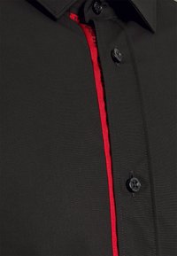 Zwarte shirt met een verticale rode streep langs de knoopsluiting. Kenmerkt zich door zwarte knopen en een gladde, matte textuur. Klassiek kraagontwerp.