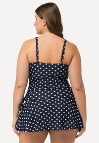 Robe de bain à pois marins avec bretelles ajustables, fronces à la taille et jupette évasée. Le tissu semble lisse avec un léger éclat.