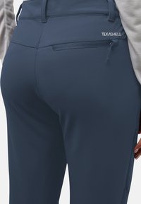 Pantalons de sport bleu marine en tissu extensible avec une texture lisse, dotés d'une poche arrière zippée et d'un détail logo le long de la taille.