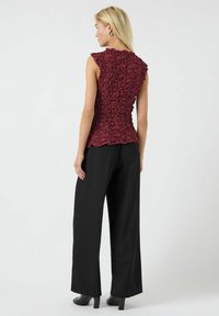 Top senza maniche bordeaux con dettagli arricciati testurizzati, abbinato a pantaloni neri a gamba larga e scarpe con tacco alto. Visuale posteriore mostrata.