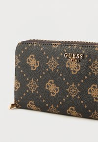 Čierna peňaženka z umelej kože s reliéfnym zlatým logom a vzormi. Má zipsové zapínanie a uhlové zlaté ozdoby na okrajoch.