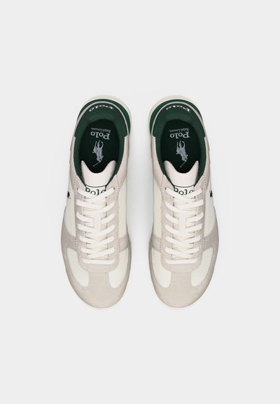 Paire de baskets Polo Ralph Lauren blanches et beiges avec des lacets blancs, une doublure intérieure verte, et le logo de la marque sur les semelles intérieures et le côté.