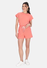 Koralfarvet tekstureret to-delt sæt bestående af en kortærmet top og shorts med snoretræk. Kombineret med hvide sneakers.
