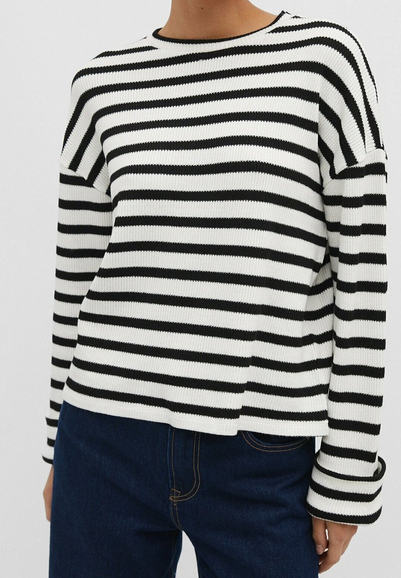 Pull en tricot rayé noir et blanc avec un col rond, des manches longues et une coupe décontractée ; le tissu présente une texture côtelée et une légère élasticité.