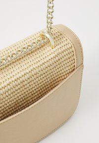 Borsa in paglia intrecciata con un lato in cuoio beige, dotata di una tracolla in catena dorata e un texture liscia, che evidenzia un effetto ombré gradiente.