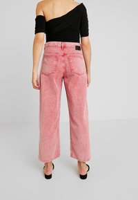 Weite, verblasste rosa Jeans mit hoher Taille, fünf Taschen und kontrastierenden Nähdetails, von hinten gezeigt.