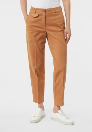 Beige Baumwollhose mit geradem Schnitt, ausgestattet mit Seitentaschen und einem einzelnen Knopfverschluss, kombiniert mit weißen Sneakern.