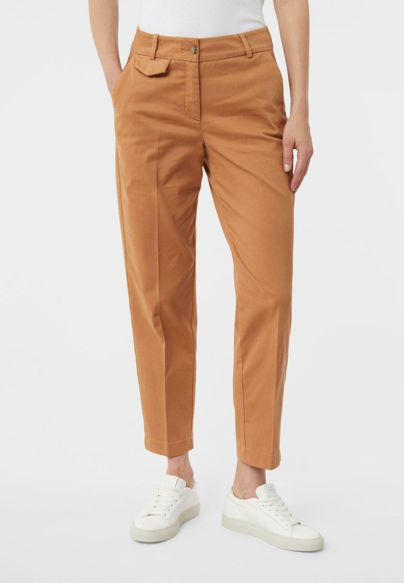 Pantaloni di cotone beige con taglio dritto, dotati di tasche laterali e chiusura con un solo bottone, abbinati a sneakers bianche.