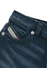 Jeans in denim blu scuro con una tasca per le monete che mostra un'etichetta ricamata della Diesel Industry e bottoni in metallo a rivetto sulla cintura.