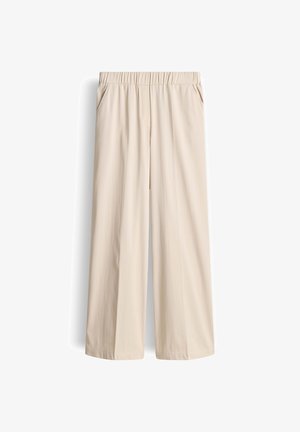 Beige broek met wijde pijpen, elastische tailleband en zijzakken, afgebeeld tegen een witte achtergrond.