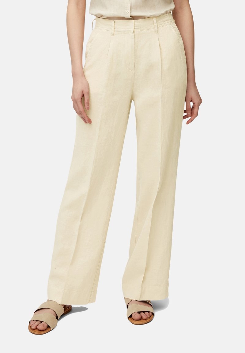 Crème-kleurige linnen broek met een ruime pasvorm, voorzien van voorplooien en een hoge taille. Gecombineerd met beige platte sandalen.