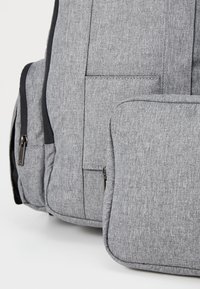 Γκρίζα σακίδιο καμβά με υφή, διαθέτοντας μπροστινή τσέπη και αποσπώμενη μικρότερη θήκη με φερμουάρ.