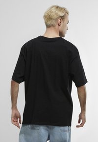 Černé oversized tričko s krátkým rukávem, vyrobené z bavlny. Obsahuje kulatý výstřih a uvolněný střih, nošeno s světle modrými džíny.