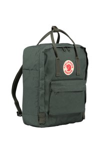 Sac à dos vert en tissu résistant, de forme carrée, avec une poche frontale, des poignées supérieures, des bretelles et une étiquette logo circulaire.