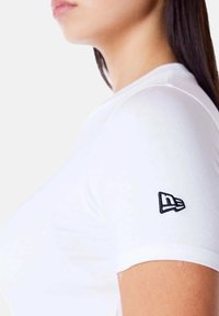 Witte aansluitende T-shirt met korte mouwen. Bevat een zwart geborduurd logo op de linkermouw. Gemaakt van een gladde, zachte stof.