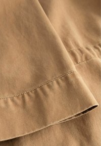 Khaki tkanina s hladkým povrchom, s priamymi švami a jemným leskom. Záhyb odhaľuje čisté okraje a detaily šitia.