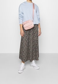 Borsa a tracolla rosa con finitura testurizzata. Indossata sopra un maglione azzurro chiaro e una gonna midi nera con motivo floreale. Abbinata a sneakers bianche alte.