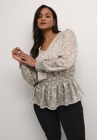 Blusa grigia chiara con motivo, in tessuto trasparente, vita arricciata e maniche a sbuffo; abbinata a pantaloni neri. Presenta sottili righe e un design floreale.