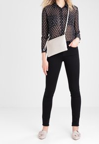 Blusa trasparente nera a pois, pantaloni neri aderenti, borsa a tracolla grigio chiaro e mocassini beige con dettaglio annodato.