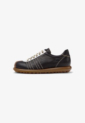 Black and white leather shoe with a low profile, featuring brown rubber sole, beige laces, and stitch detailing on the upper.
