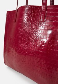 Rode patenten nepleren krokodillen leren tote bag met het geïmplodeerde "TED BAKER LONDON" logo, voorzien van twee platte handvaten en een gestructureerd ontwerp.