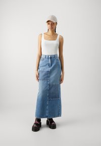 Denim maxi skjørt med lappemønster, med høy midje, lyseblå farge og frynset kant. Brukt med en hvit tank topp og caps.