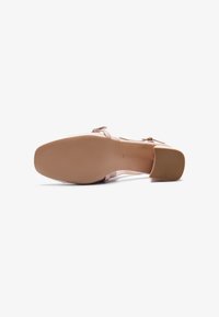 Escarpin à talon haut rose avec une bandoulière transparente et une semelle en caoutchouc beige clair. Dispose d'un talon bloc et d'un design minimaliste.
