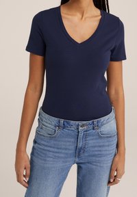 Marinblå V-ringad t-shirt tillverkad av mjuk bomull, korta ärmar, figurnära design, ihop med slitna ljusblå jeans.