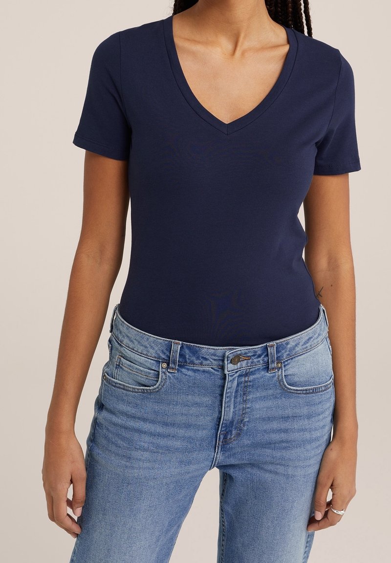 Marinblå V-ringad t-shirt tillverkad av mjuk bomull, korta ärmar, figurnära design, ihop med slitna ljusblå jeans.