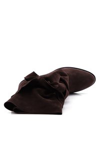 Botín ankle de ante marrón con un eje suave y gathered, y un prominente detalle de lazo en la parte frontal, con puntera afilada y suela negra.