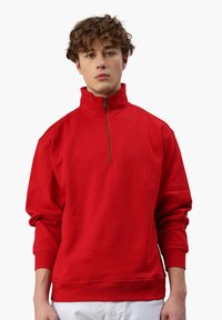 Roter Pullover mit hohem Kragen und halbem Reißverschluss. Aus glattem Stoff gefertigt, mit langen Ärmeln und gerippten Bündchen.