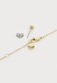 Goldkette mit einem hexagonalen Charm, silberner Steckerohrring und einer metallischen Ohrmanschette. Jedes Stück weist unterschiedliche Materialien und Oberflächen auf.