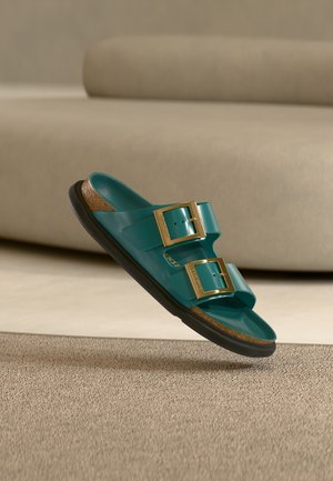 Τυρκουάζ σανδάλια με λουράκια και δύο χρυσά κούμπωματα, πάτος από φελλό και μαύρη ελαστική σόλα. Λείο υφή, ανοιχτό σχέδιο και επίπεδη σιλουέτα.