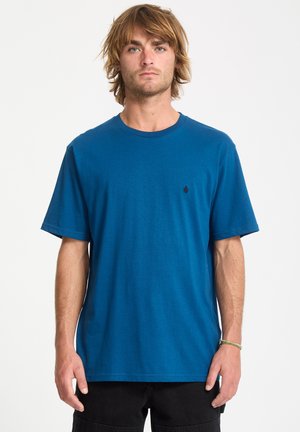 T-shirt en coton bleu avec un col rond et des manches courtes. Présente un petit logo noir sur la poitrine gauche. Texture lisse, coupe décontractée.