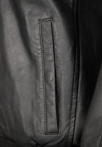 Nahaufnahme einer schwarzen Lederjacke mit glatter Oberfläche, vertikalem Taschen, dezentem Nähen und taillierter Passform.