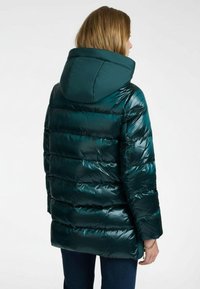 Tyrkisturquoise donzenjas met een glanzend, gewatteerd design en een capuchon. Heeft horizontale stiksels en een ontspannen pasvorm. Het materiaal lijkt glad en flexibel.