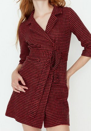 Wikkeljurk met rood-zwart pied-de-poule patroon, driekwart mouwen, tailleband en een kraag. Gemaakt van gestructureerde stof.