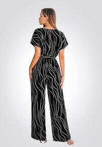 Combinaison noire avec des jambes larges fluides, ornée de motifs en vagues blanches. Dispose de manches courtes, d'une taille ceinturée et d'un dos en trou de serrure.
