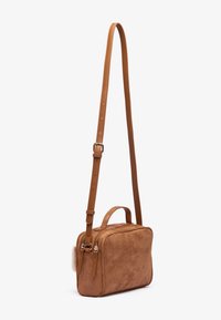 Sac bandoulière en daim beige avec une poignée supérieure, une bandoulière ajustable, une fermeture à double zip et un accent en fourrure douce sur le côté.